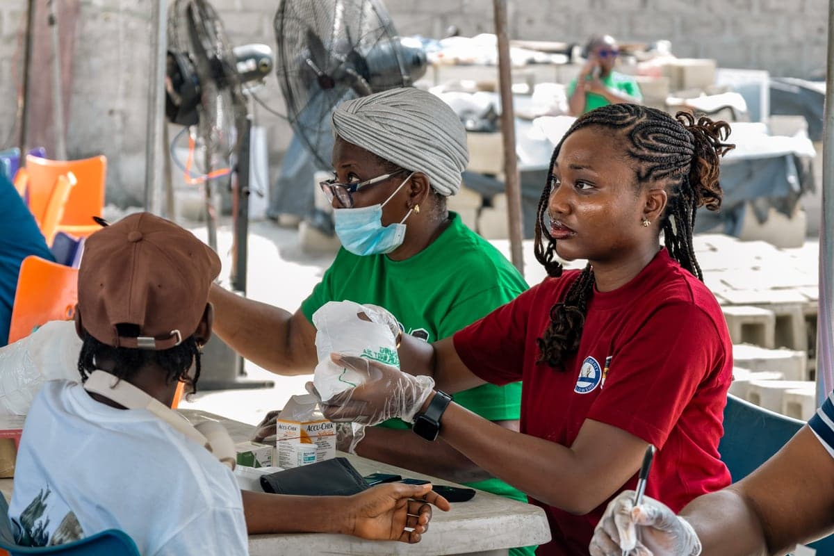 A clinician in gloves taking a blood sample from a seated patient.