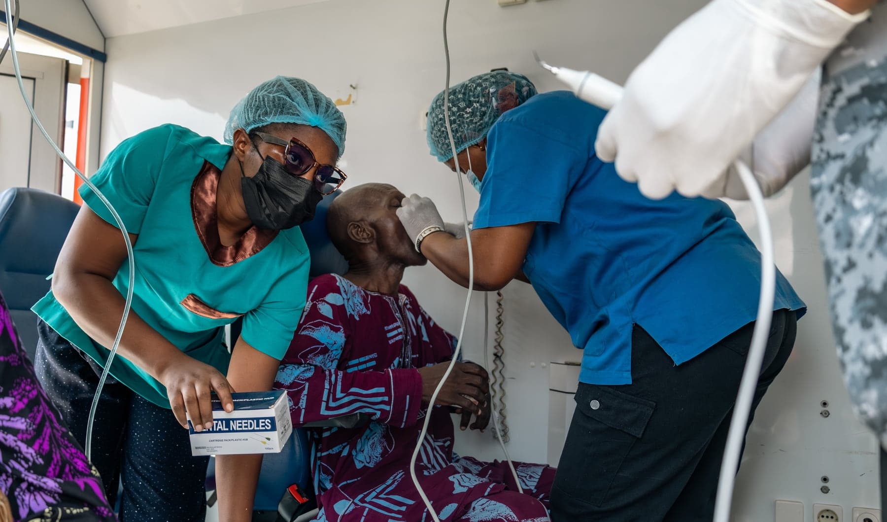 Clinicians in scrubs treating a seated patient at the outreach.